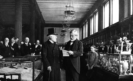 1870年から1905年までユニオン・スクエアに店を構えていた頃のティファニー。87歳のチャールズ・ルイス・ティファニー（右）が顧客とやり取りしている。店内には贅沢な品々がズラリ。©The Jewelers’ Circular